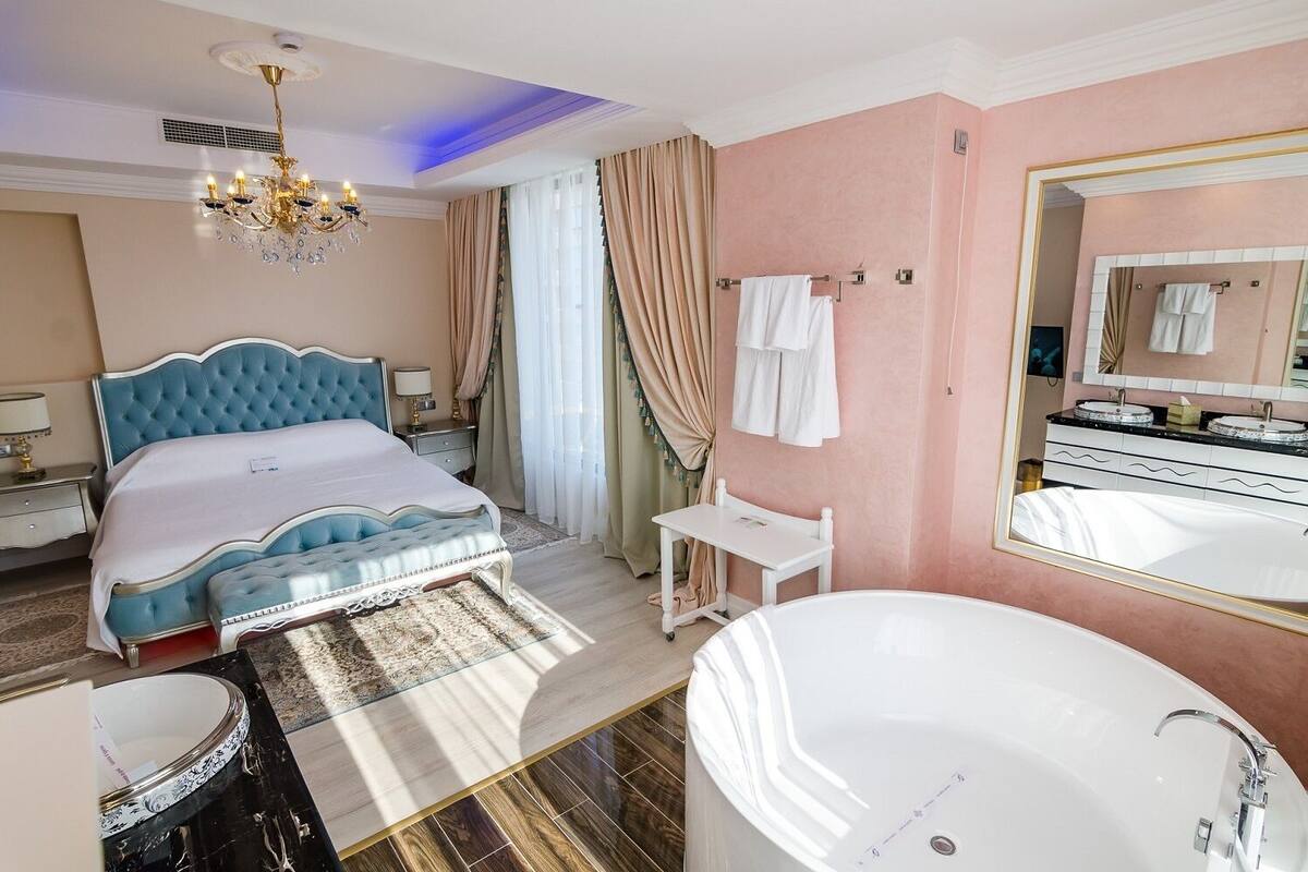 A bedroom with a large bed, a sitting area, a bathroom with a bathtub, and a vanity with a mirror.