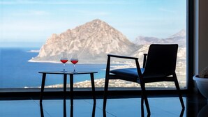 A room with a view of a mountain and the sea, a table with two glasses of red wine, and a single chair. - RESORT VENERE DI ERICE HOTEL & SPA (Valderice)