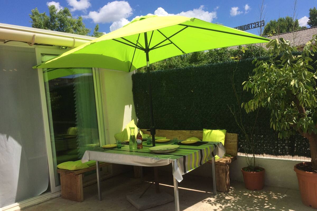 A patio with a table set for dining, a bright green umbrella, and potted plants.