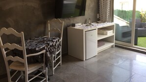 A room with a TV mounted on the wall, a desk with a chair, and a view of a garden through a sliding glass door. - Les Chambres de Naevag (St.-Rémy-de-Provence)