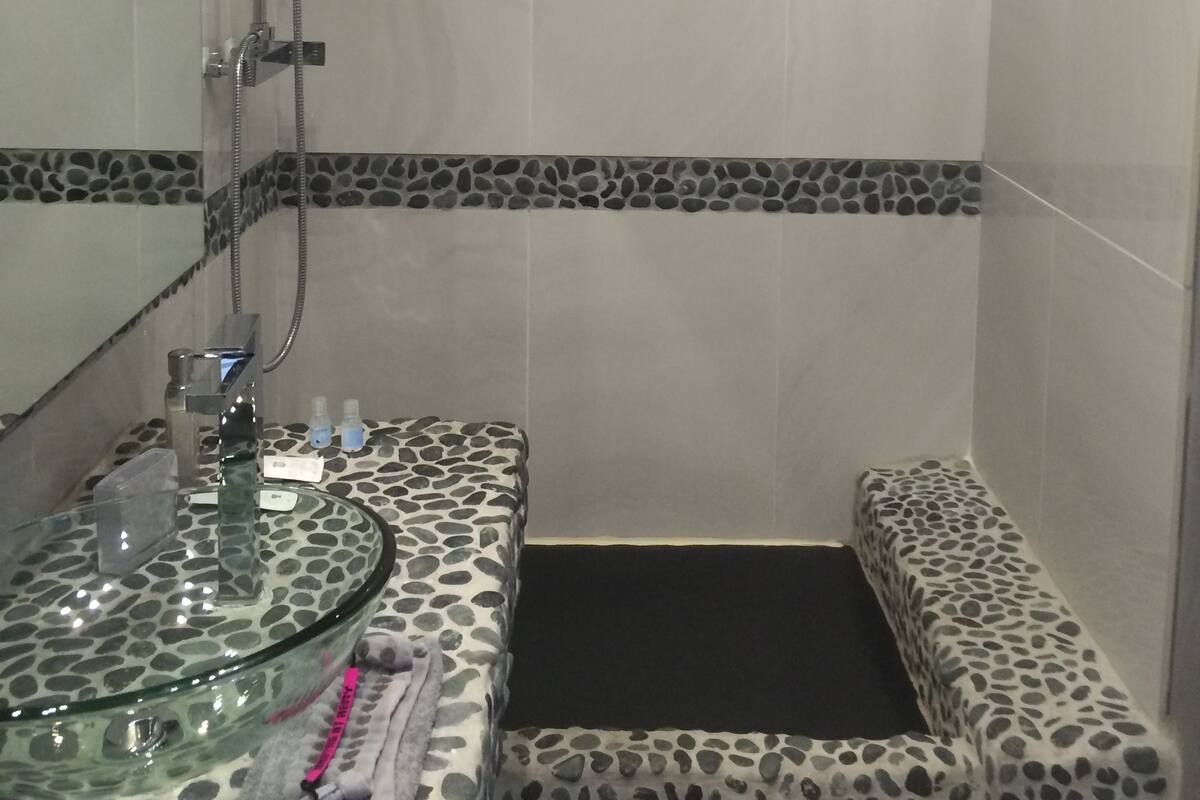 A bathroom with a glass basin, a shower, and a bench.