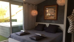 A modern bedroom with a large bed, a bench, a hot tub, and a view of greenery outside. - Les Chambres de Naevag (St.-Rémy-de-Provence)