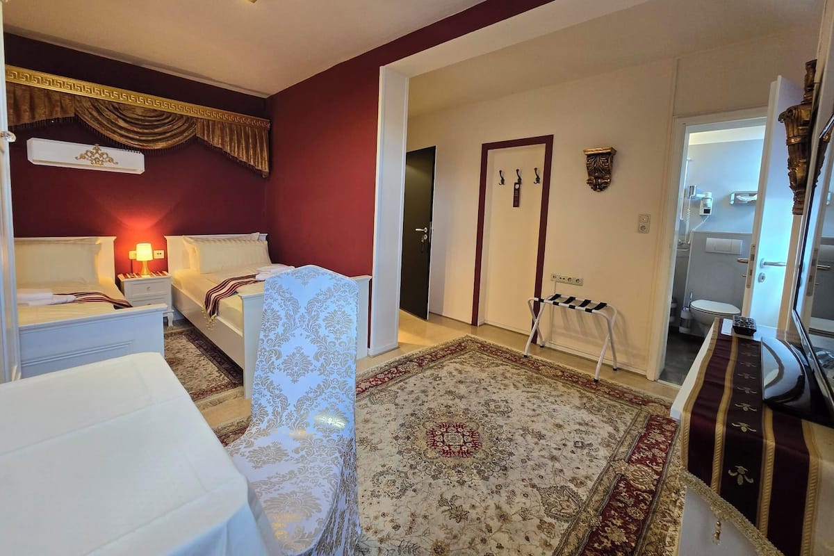 A hotel room with two beds, a sitting area, a bathroom, and a small sitting area with a chair.