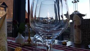 A wine glass on a table with a red and white striped tablecloth, a lamp, and a view of a building through a window.