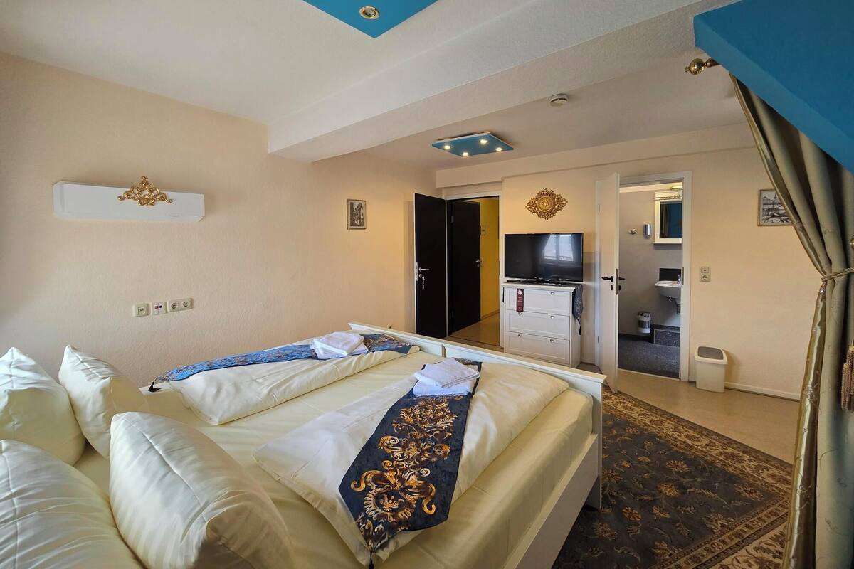A hotel room with two beds, a TV, a minibar, and a bathroom visible through an open door.
