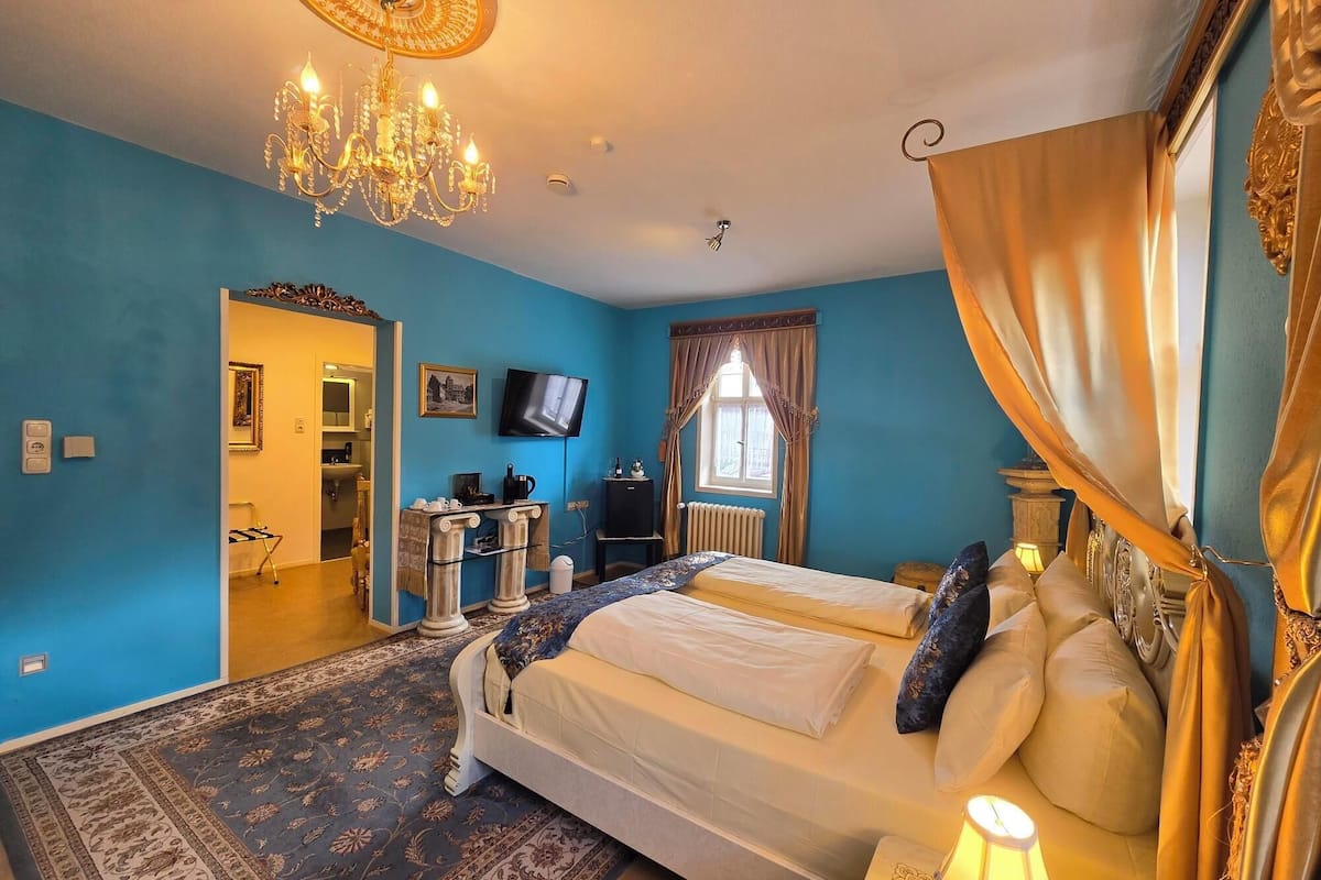 A hotel room with two beds, a chandelier, a television, and a view of the outside through a window with curtains.