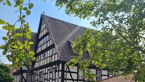 Un edificio tradicional de entramado de madera con un letrero que indica que es un hotel. Hay coches aparcados delante y el edificio está rodeado de árboles.