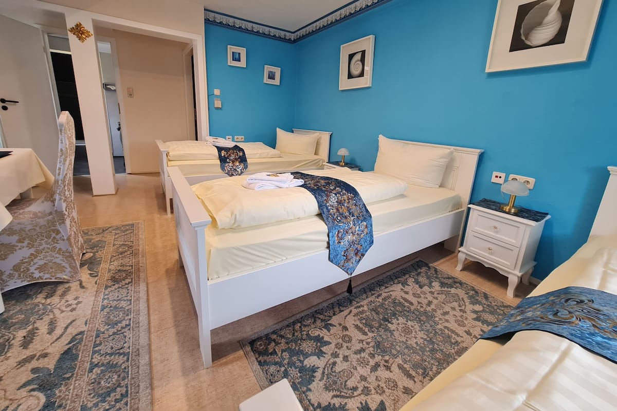 A hotel room with three beds, a blue accent wall, and a patterned rug.