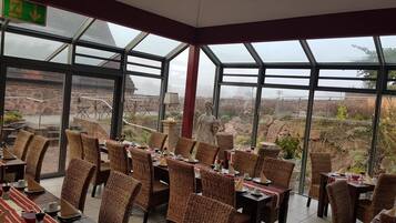 En restaurang med möbler i rotting, både stolar och bord, och stora fönster som ger utsikt över ett kargt landskap.