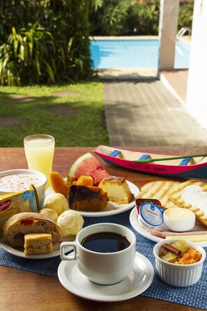 A breakfast table with a variety of food items including bread, fruit, and a cup of coffee. - Pousada Recanto da Ladeira (Paraty)