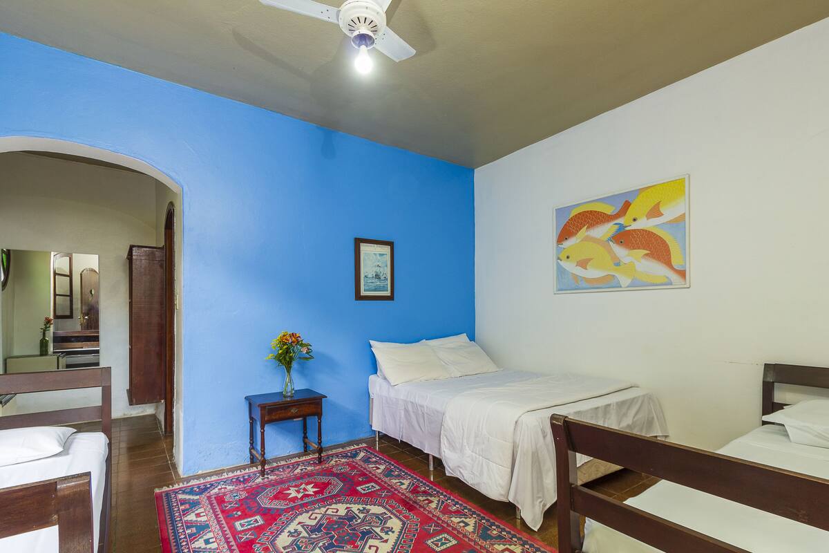 Une chambre avec un mur bleu, un lit, une petite table sur laquelle se trouve un vase, et un tableau.
