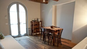 A room with a wooden dining table, chairs, a sofa, and a large arched window. - Azienda Agricola Baccagnano (Brisighella)