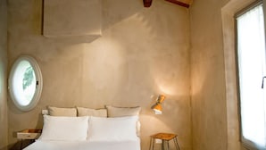 A bedroom with a bed, a nightstand, a small stool, a wall-mounted lamp, and a window. - Azienda Agricola Baccagnano (Brisighella)