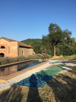 Uma piscina com tapete azul estampado, um edifício com telhado telhado e uma árvore ao fundo.