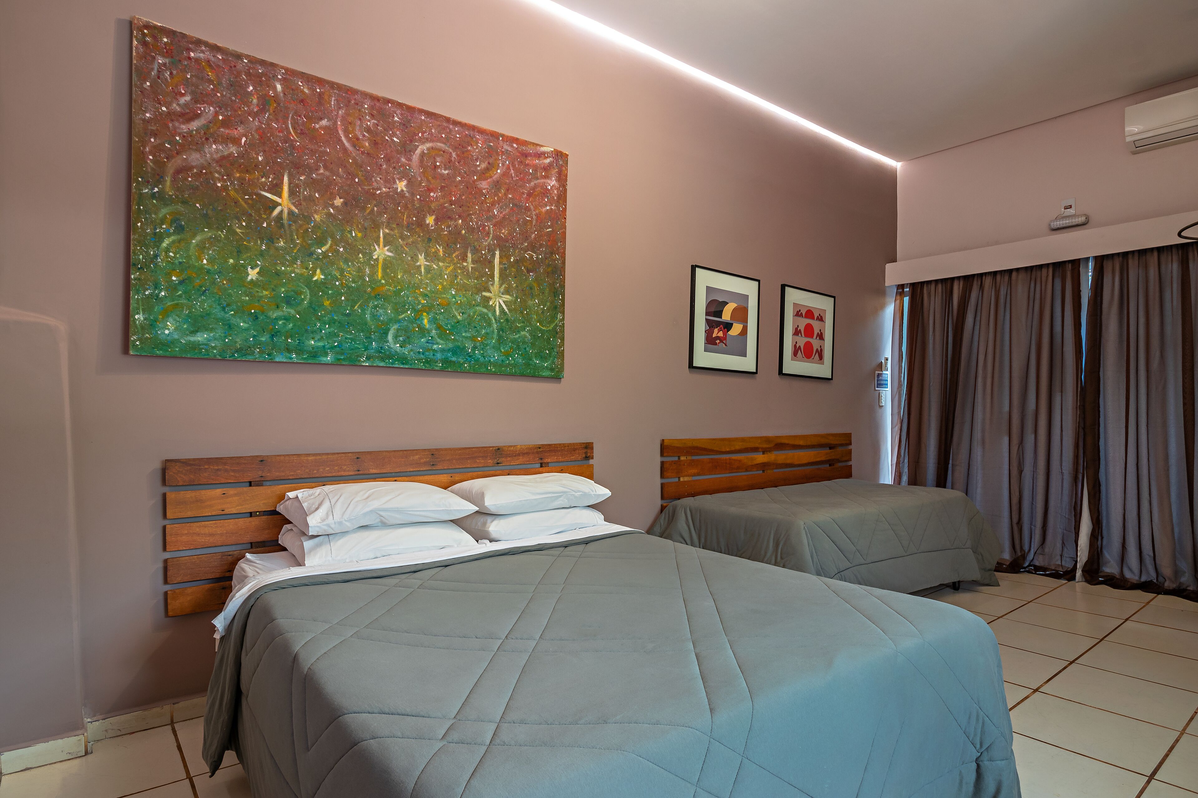 A hotel room with two beds, a large abstract painting, and two framed pictures on the wall.