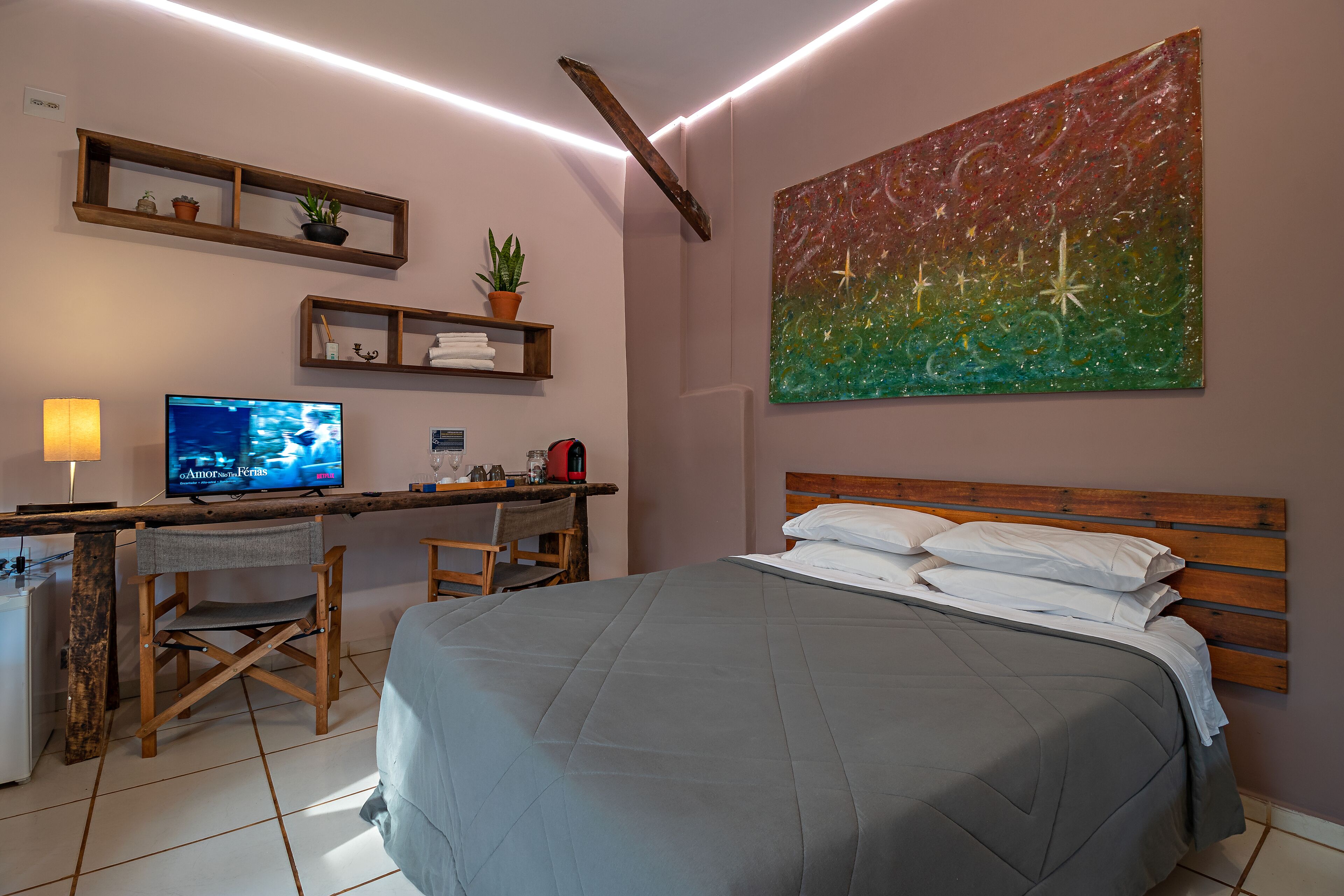 A bedroom with a bed, a desk with a computer, and a painting on the wall.