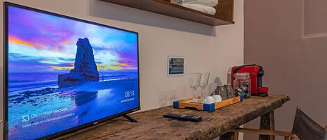 A television displaying a sunset scene, a remote control, a tray with glasses and a jar, and a wooden shelf with towels.