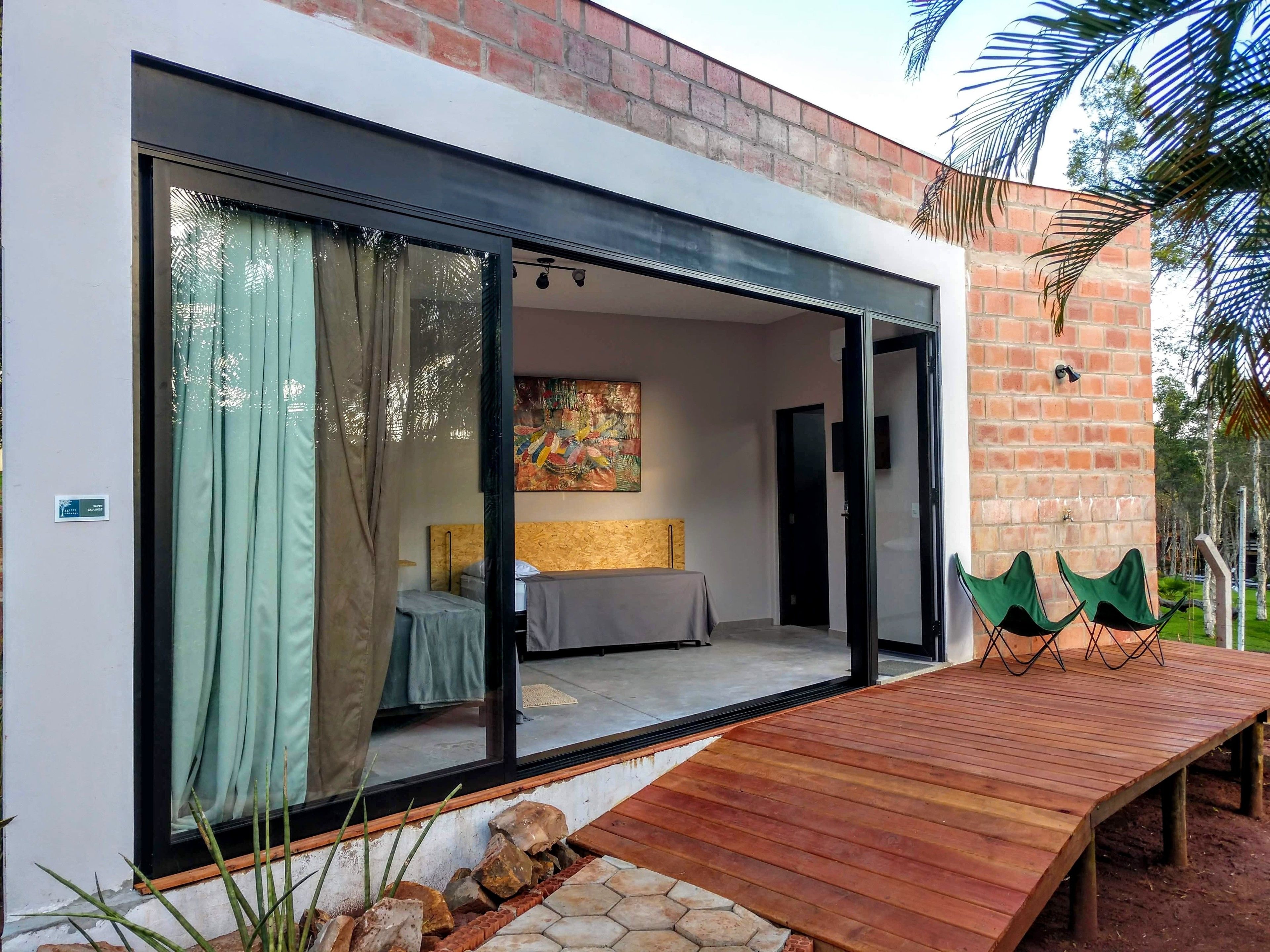 Una habitación moderna con un gran ventanal corredera, una cama, un banco de madera y vistas al exterior.