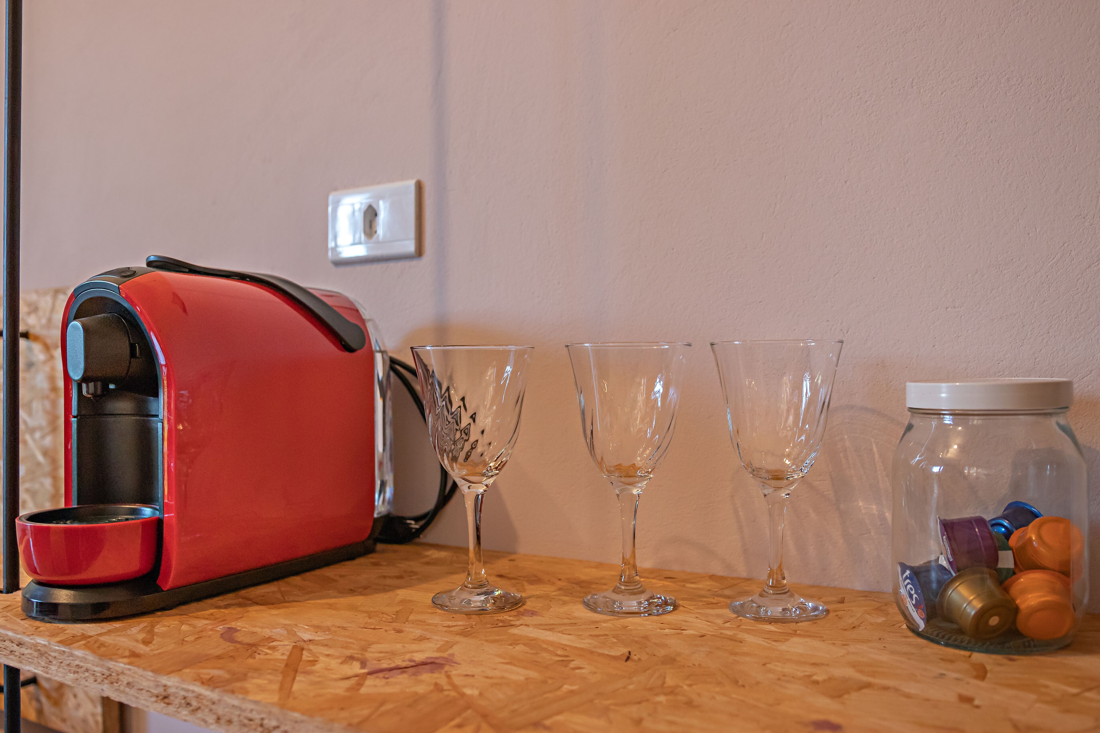 En køkkenbordplade med en rød toaster, tre vinglas og et glas med farvede låg.