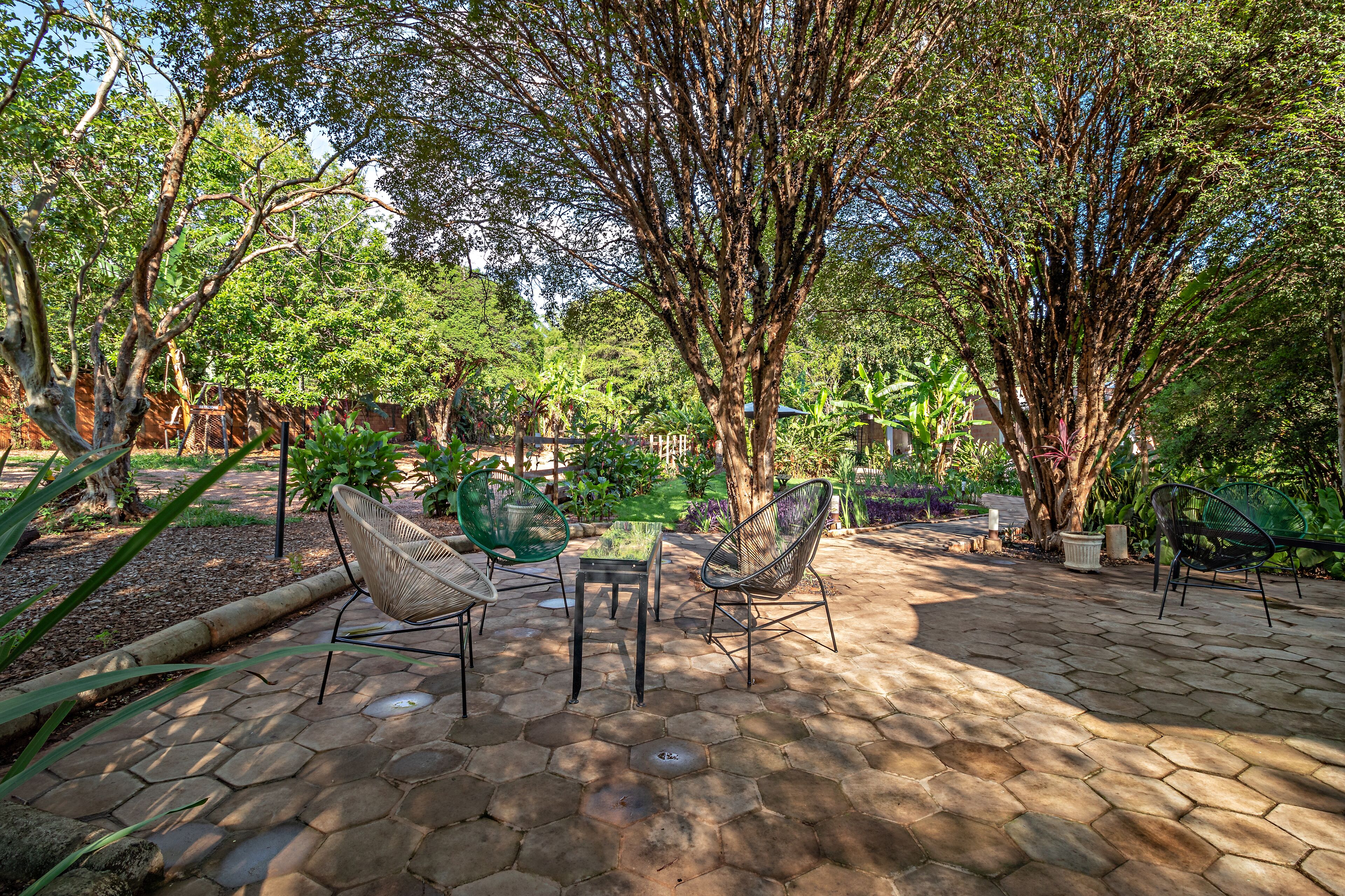 An outdoor patio area with hexagonal stone flooring, surrounded by lush greenery and trees.