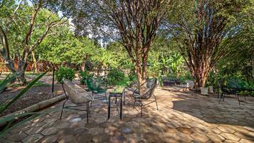An outdoor patio area with hexagonal stone flooring, surrounded by lush greenery and trees.