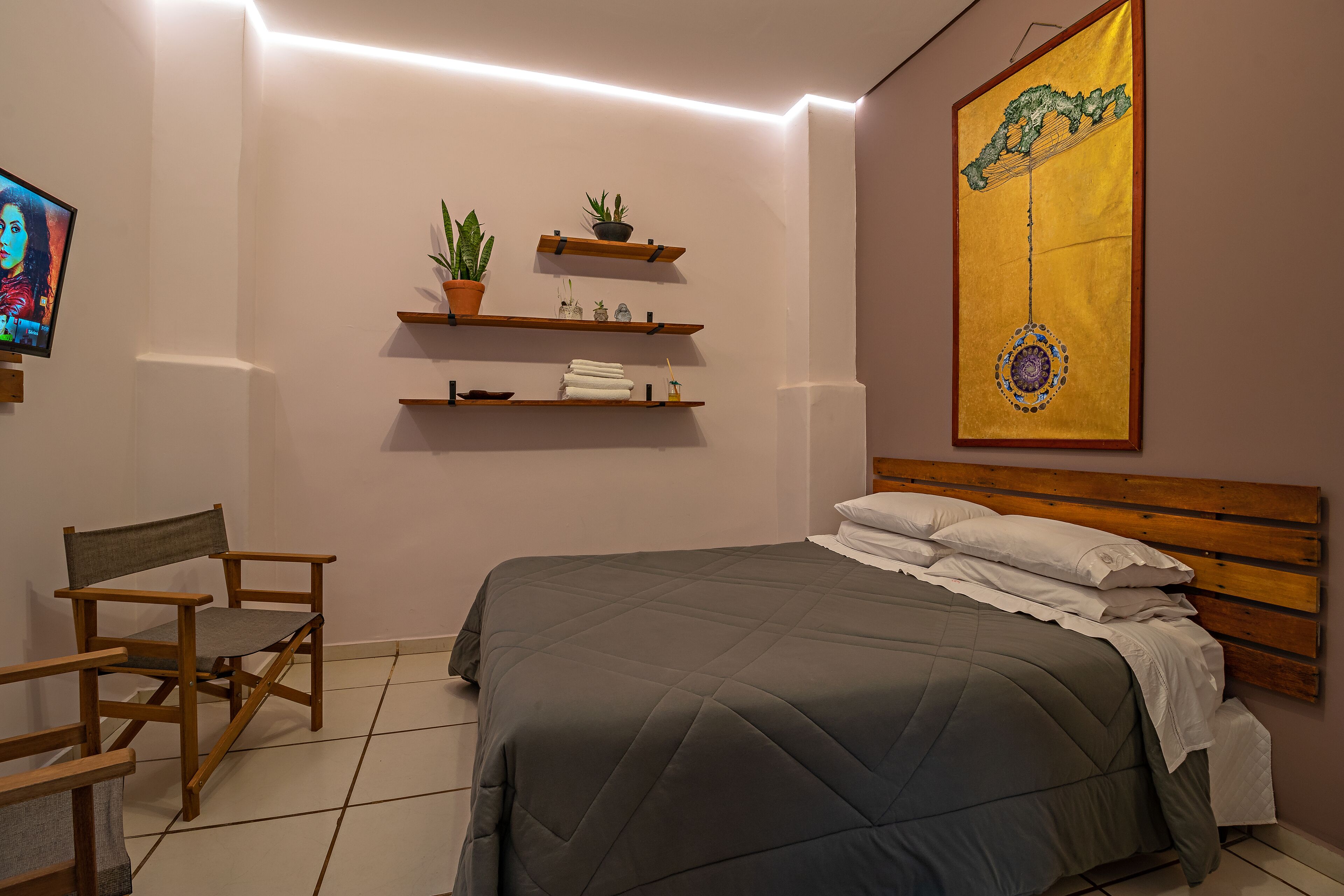 A bedroom with a bed, a chair, shelves with plants, and a painting on the wall.