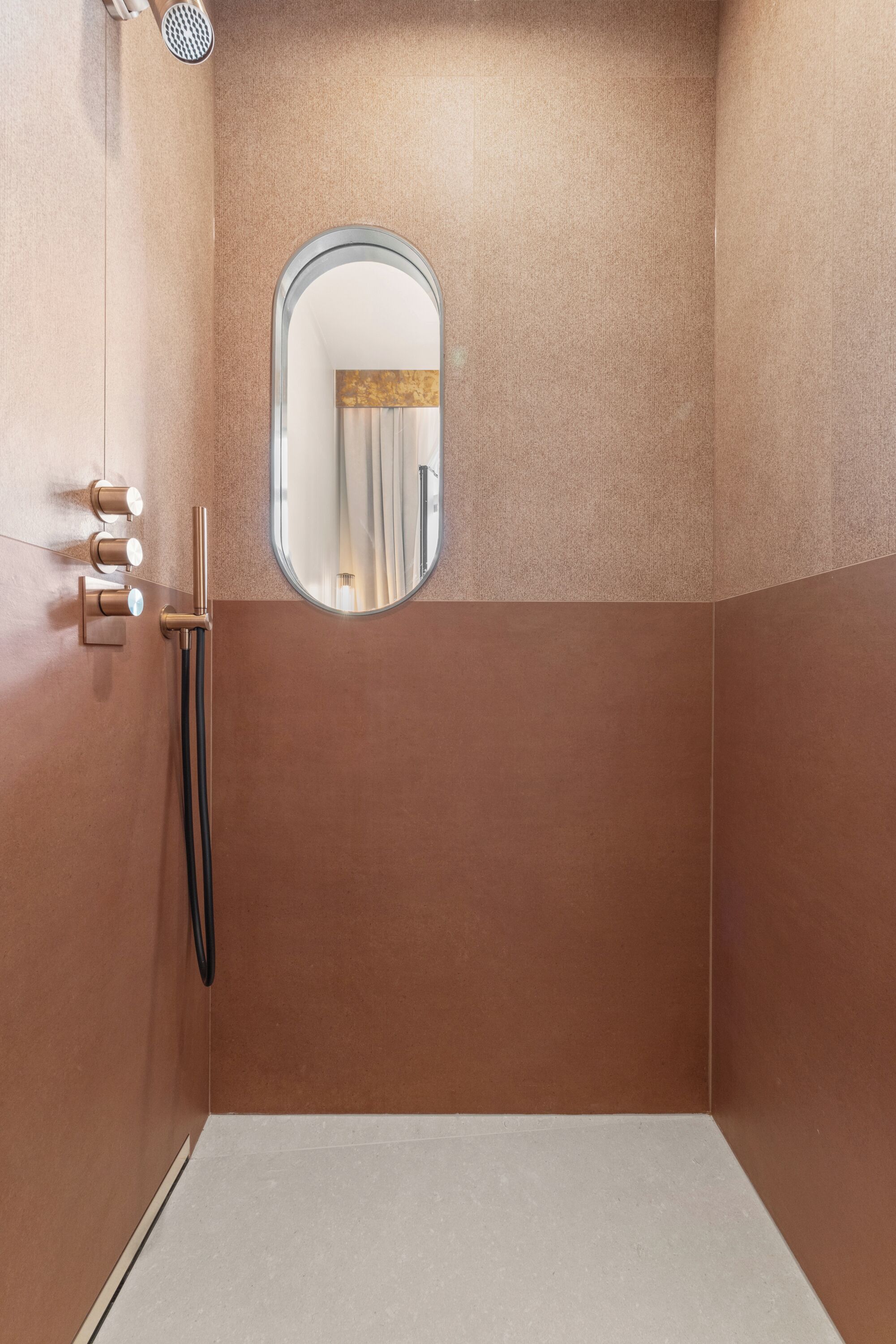 Una ducha con cabezal de ducha manual, grifo de pared y un espejo pequeño.
