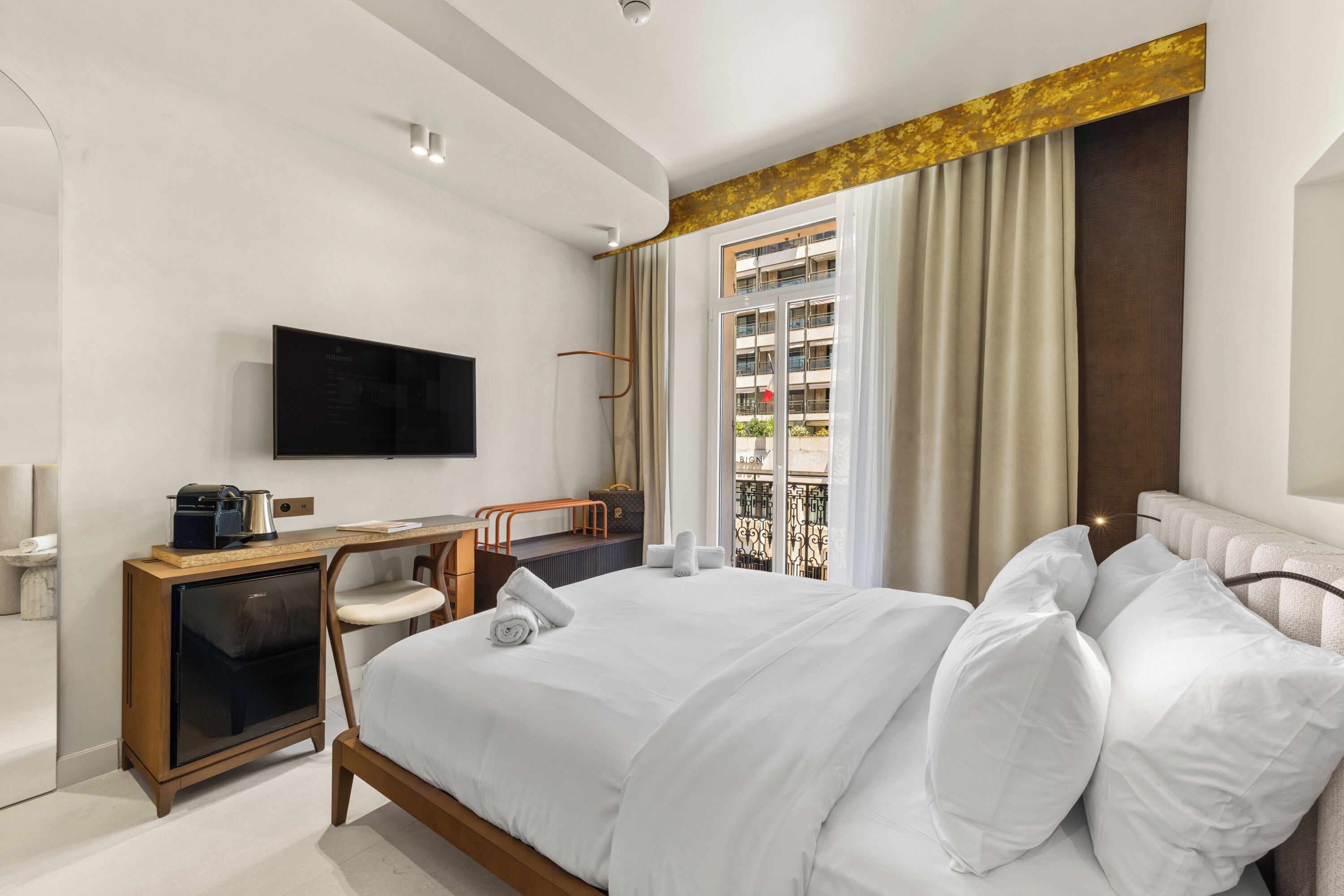 A modern hotel room with a bed, a desk, a television, and a window with curtains.