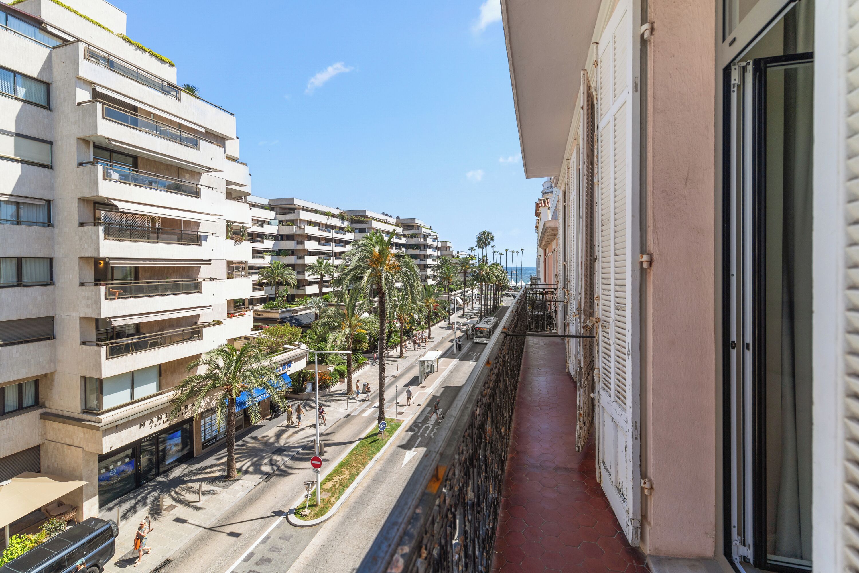 A balcony overlooking a street with buildings, palm trees, and a clear sky.