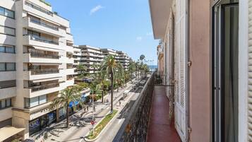 A balcony overlooking a street with buildings, palm trees, and a clear sky.