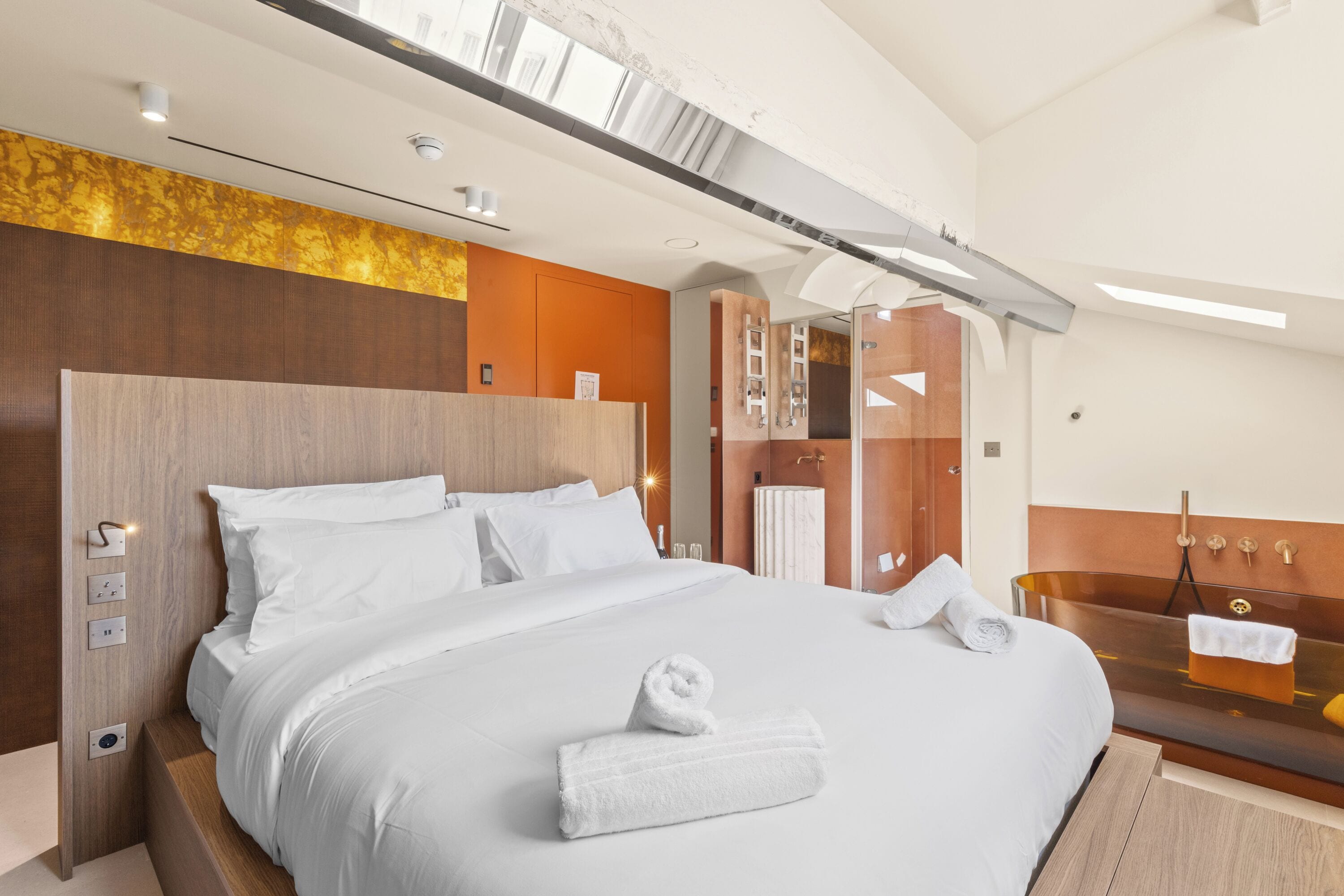 A modern hotel room with a large bed, a built-in bathtub, and a wooden headboard.