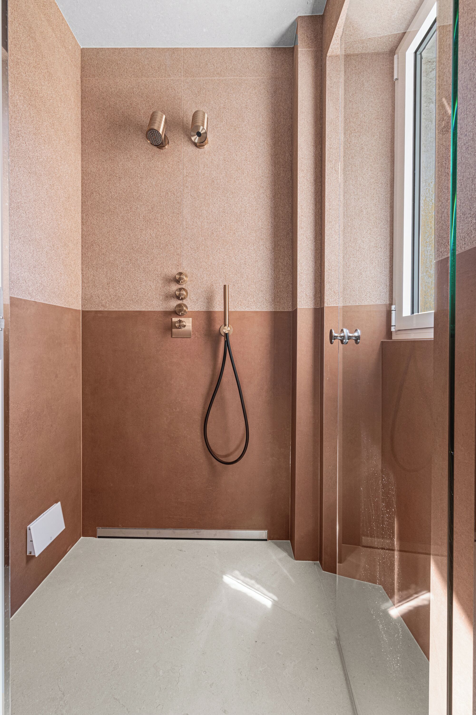 Een douche met een glazen deur, een handdouche en een bedieningspaneel aan de muur.