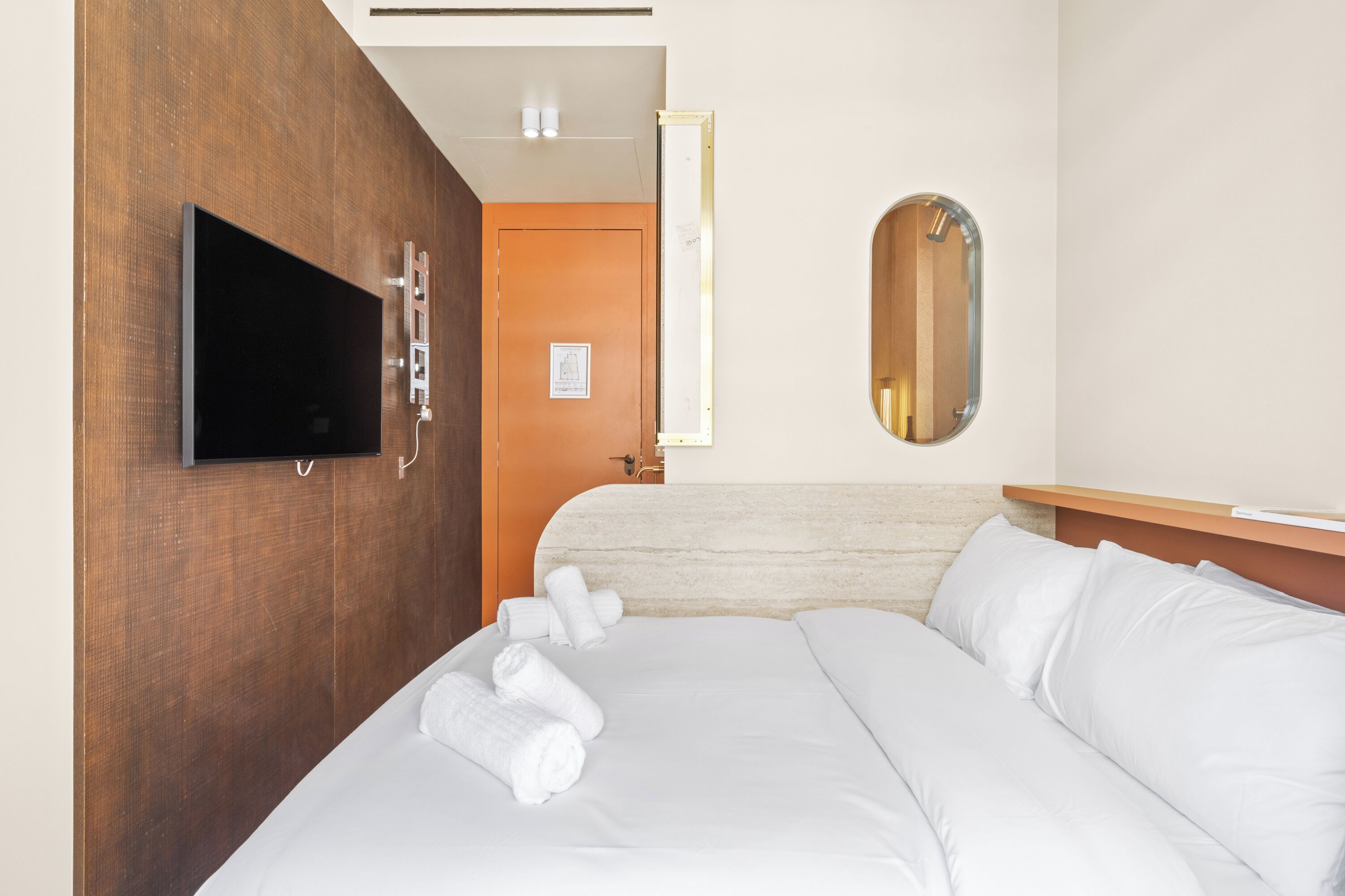 Una camera d'albergo con un letto, una TV a schermo piatto fissata al muro, una testiera in legno e uno specchio.