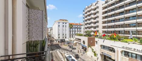 A multi-story building with balconies, a tram, and a car parked in front.