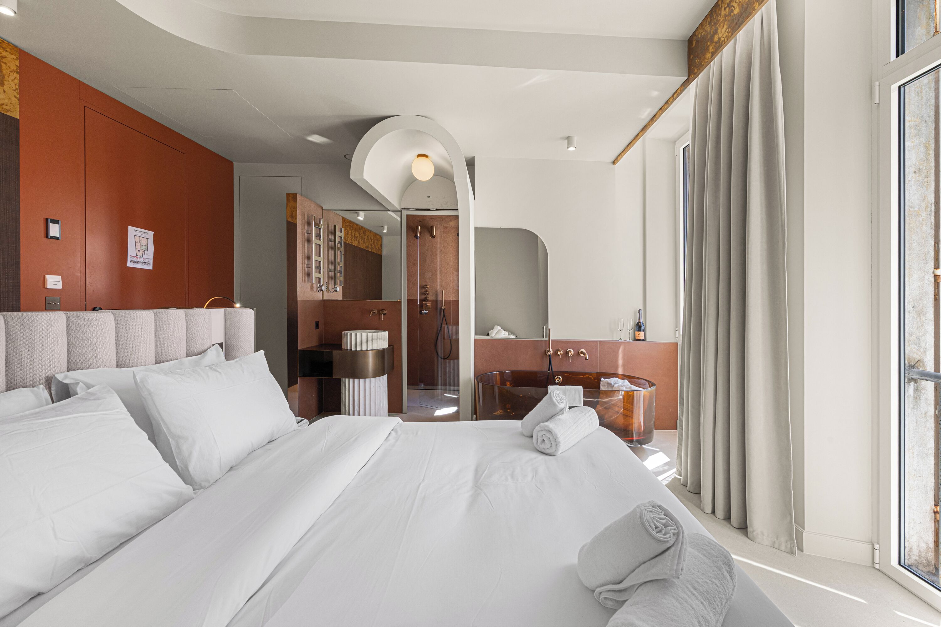 Ein Hotelzimmer mit einem großen Bett, einem Badezimmer inklusive Dusche, Waschtisch und einem Fenster mit Vorhängen.