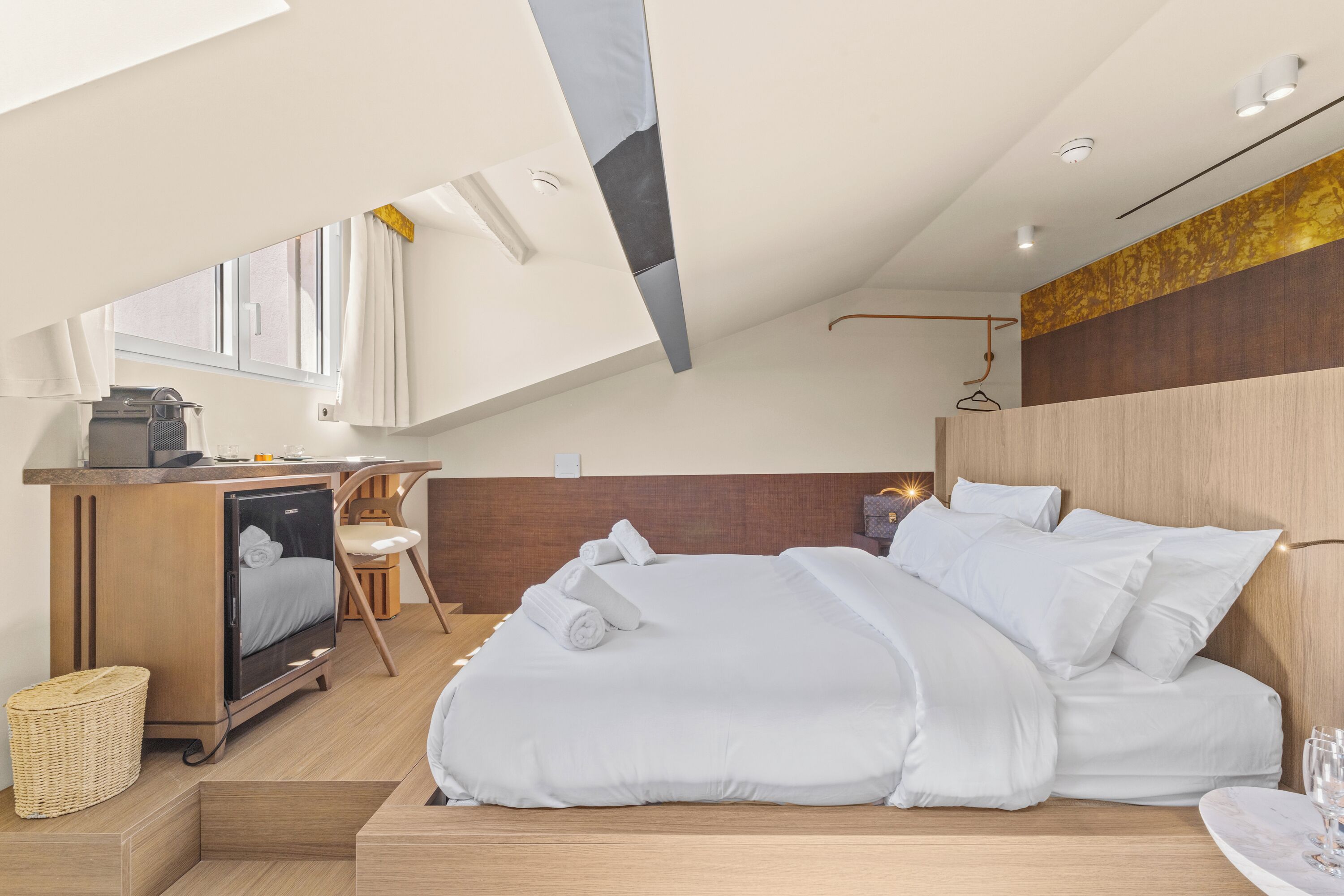 Una habitación de hotel moderna con cama, escritorio, silla, kitchenette pequeña y ventana.
