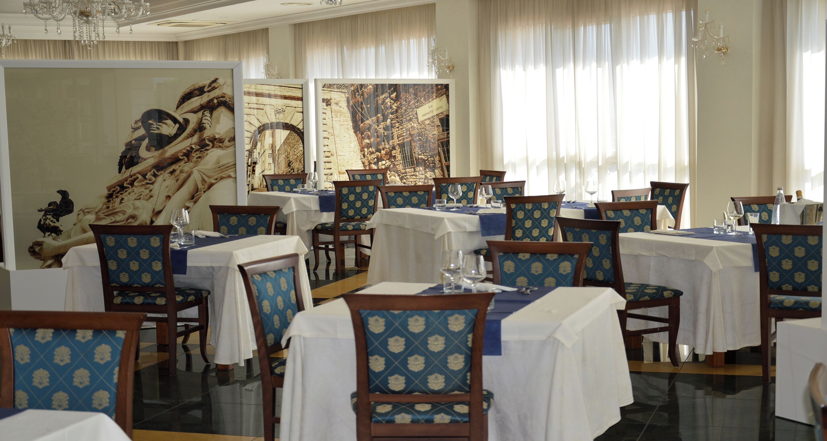 A dining area with tables set for service, chairs with patterned upholstery, and artwork on the walls.