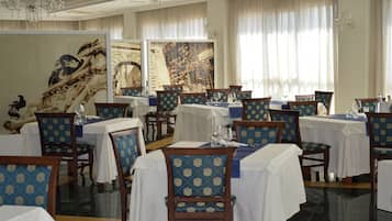 Un espace repas avec des tables dressées pour le service, des chaises dotées d’un revêtement à motifs et des œuvres d’art accrochées aux murs.
