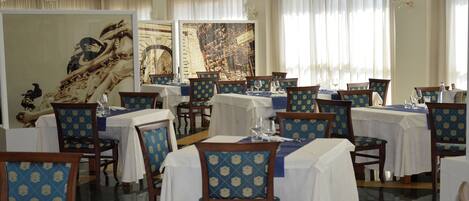 A dining area with tables set for service, chairs with patterned upholstery, and artwork on the walls.