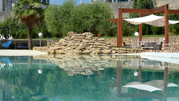 Uma área de piscina com muro de pedra, cadeiras de descanso e guarda-sóis.