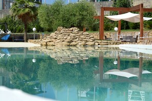Zona de piscina con pared de piedra, sillas de descanso y sombrillas.