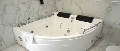 A modern bathroom with a large, curved jacuzzi tub, marble tiles, and a toilet.