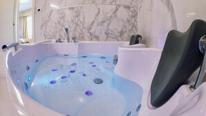 Um jacuzzi grande e moderno com um assento preto, cercado por paredes de mármore e um espelho refletindo parte do quarto.