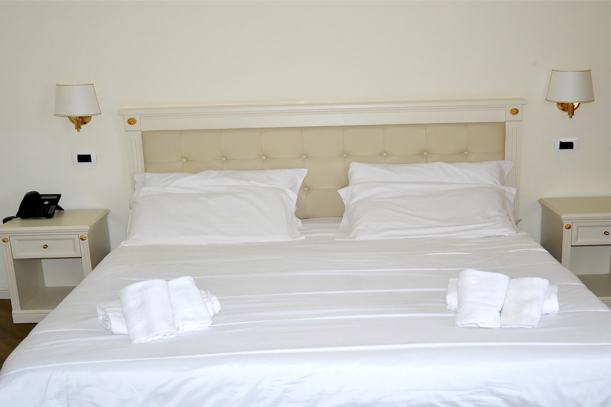 Habitación de hotel con una cama grande, dos mesitas de noche, un teléfono y dos lámparas de pared.