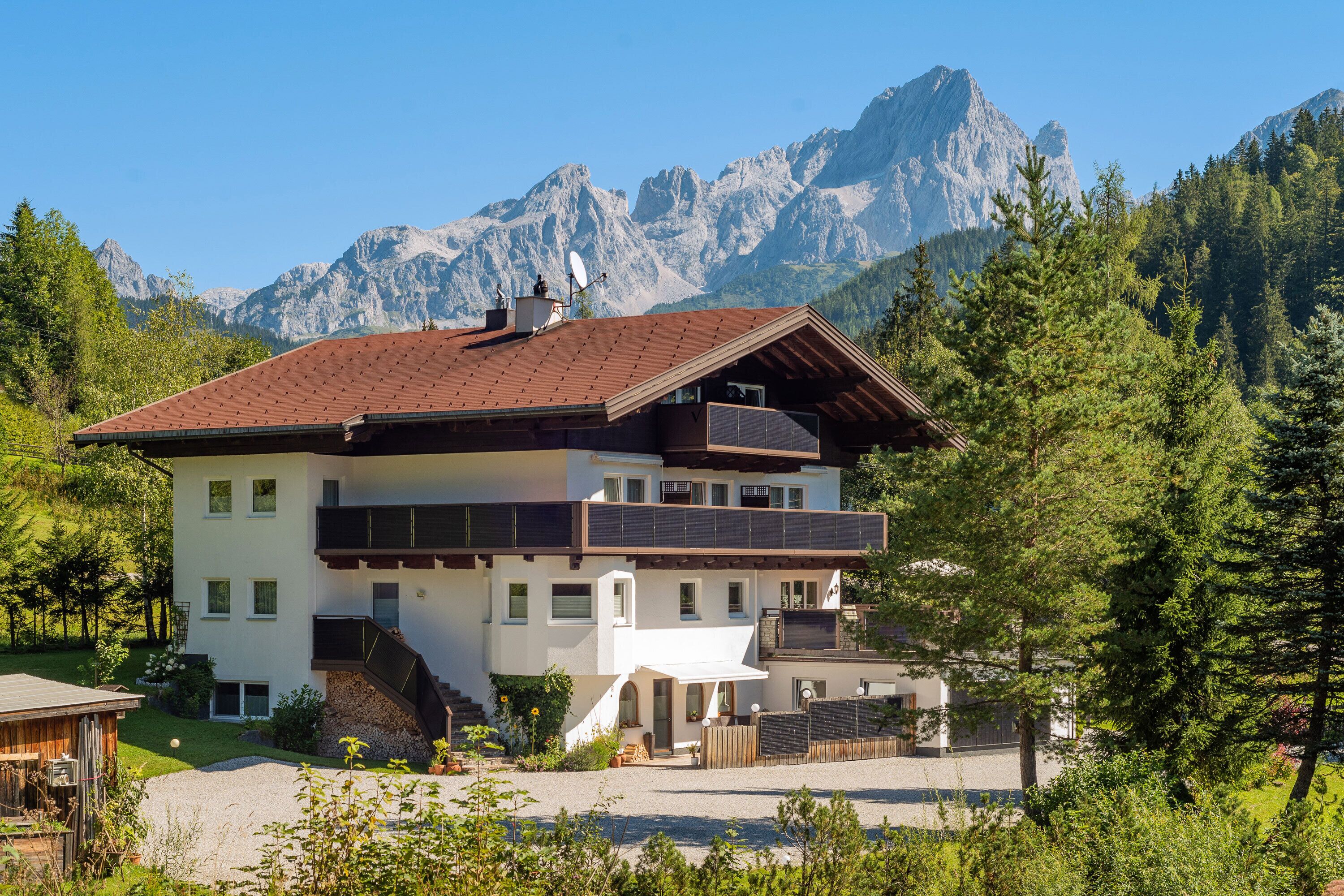 Un immeuble à plusieurs étages, doté d’un toit en pente, d’un balcon et offrant une vue sur les montagnes en arrière-plan.