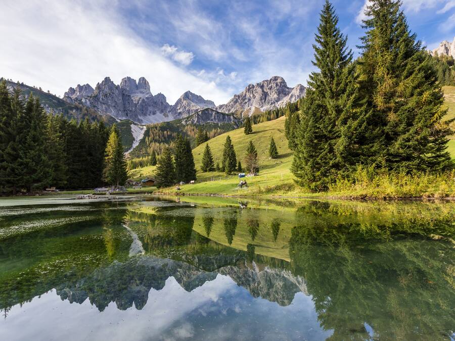 A serene lake with reflections of trees and mountains, surrounded by lush greenery and a clear sky.