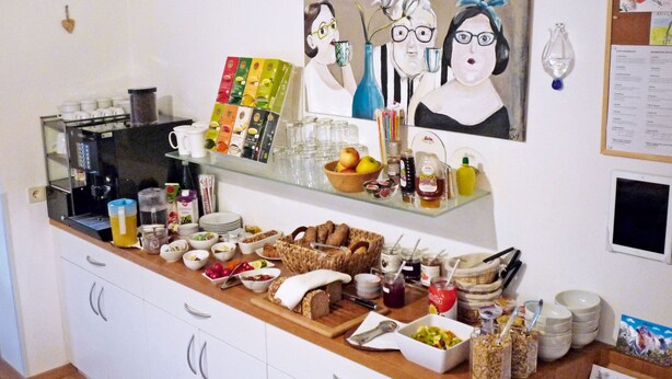 Un buffet per la colazione con diverse pietanze, una macchina per il caffè e un quadro appeso al muro.