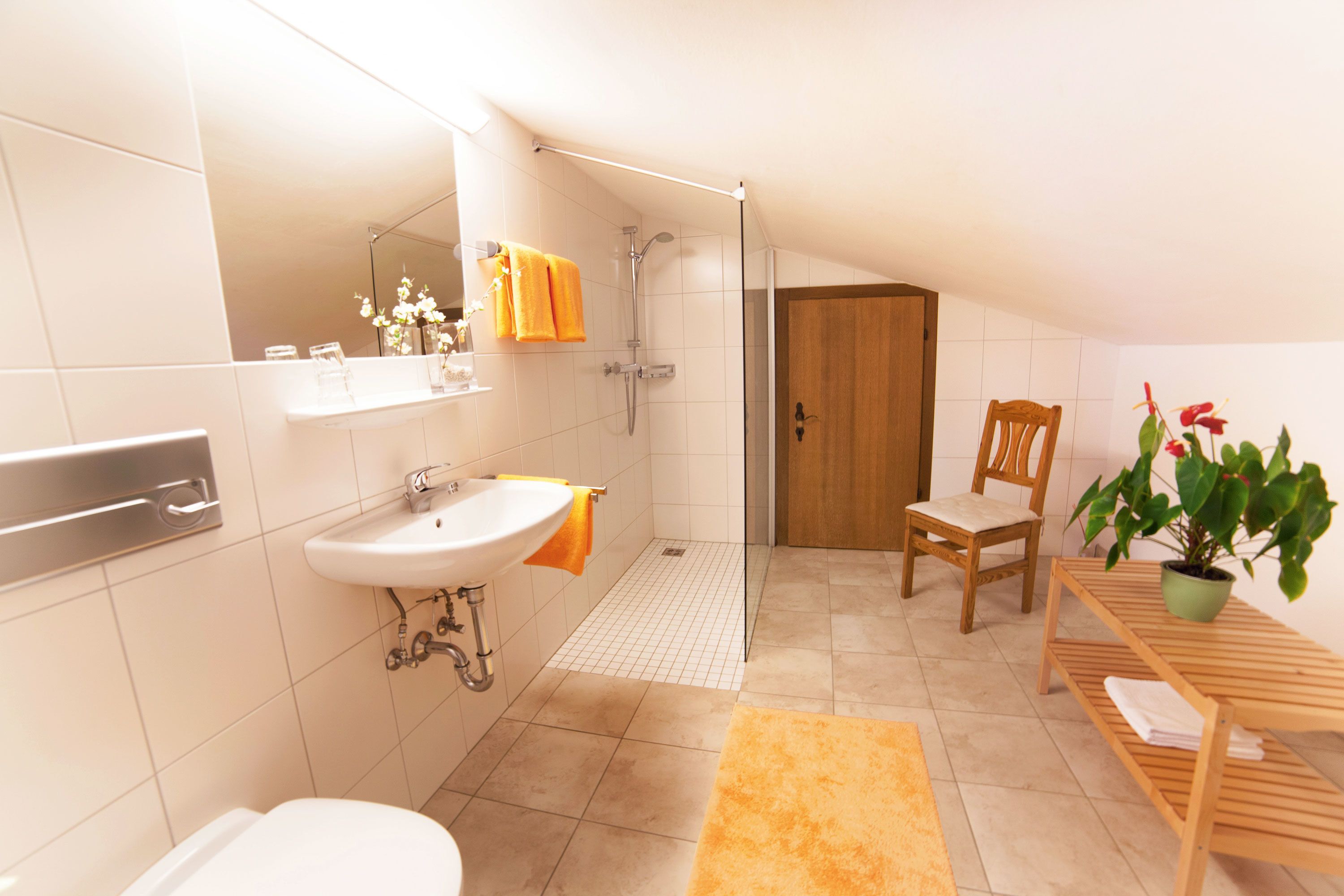 A bathroom with a toilet, sink, shower, and a chair.