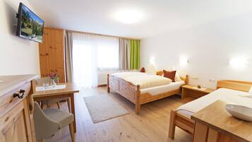 A hotel room with a wooden bed, a desk with a chair, a small table with a bowl, and a television on the wall.