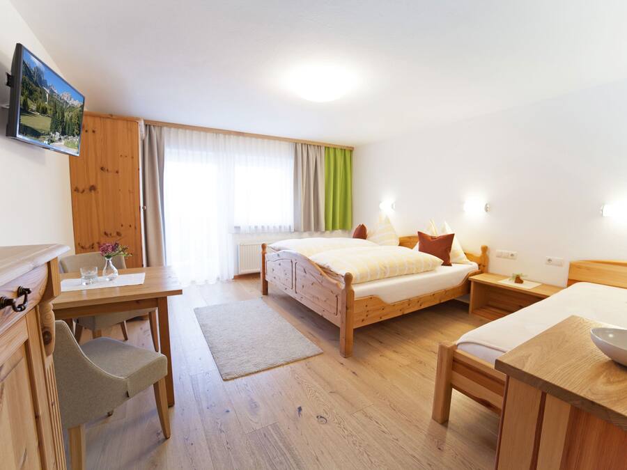 A hotel room with a wooden bed, a desk with a chair, a small table with a bowl, and a television on the wall.